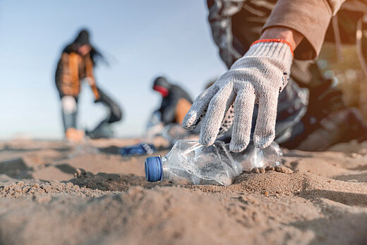 Une main gantée ramasse une bouteille de plastique sur la plage